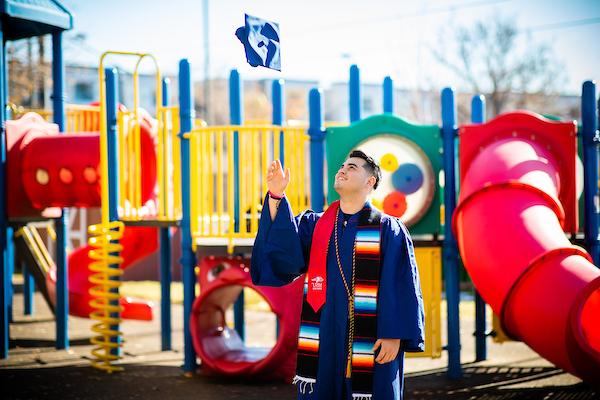 Student throwing graduation cap in front of a playground